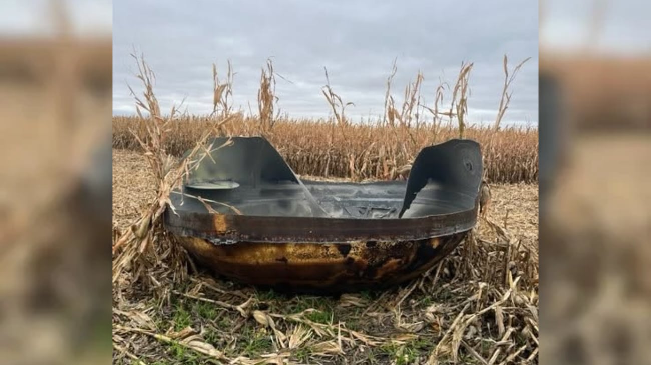 A large, scorched metallic object, roughly 11 feet in diameter, sits in a cornfield in Scott...